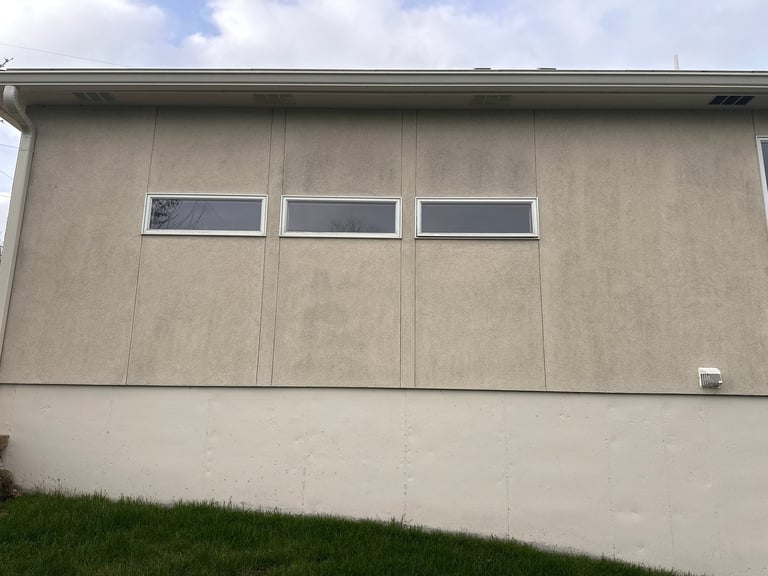 Concrete building facade with three horizontal windows and beige upper section, white lower section, against blue sky